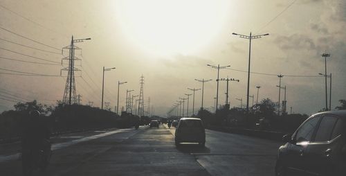 Cars on road in city against sky during sunset