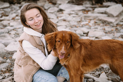 Young woman and dog retriever walks on river shore at autumn season