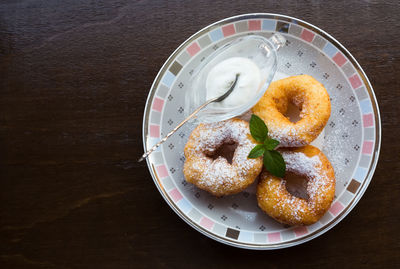 Three tasty donuts with powdered sugar, mint leaf and sour cream on plate. dark wooden background .