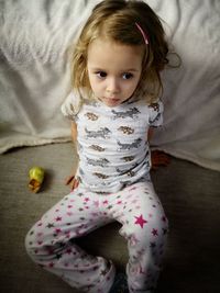 High angle view of cute girl looking away while sitting on bed at home