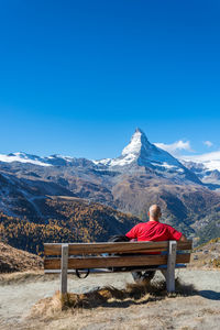 Man sitting on bench at mountain against clear blue sky