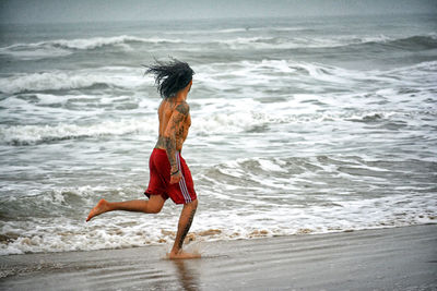 Shirtless man running at sea shore