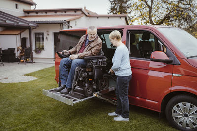 Full length of senior woman holding remote control while helping man with disability in motorized wheelchair to disembar