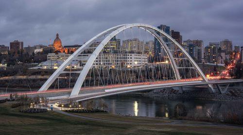 Illuminated bridge over river against buildings in city