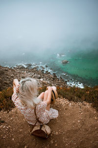 High angle view of woman sitting on cliff by sea