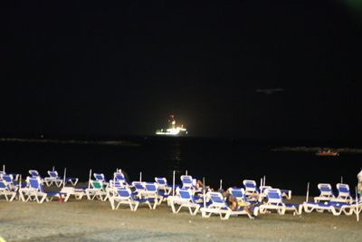 Illuminated beach by sea against sky at night