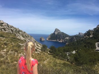 Rear view of girl standing on mountain at majorca against sky