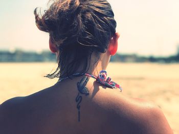 Rear view of mid adult woman in bikini standing at beach against sky