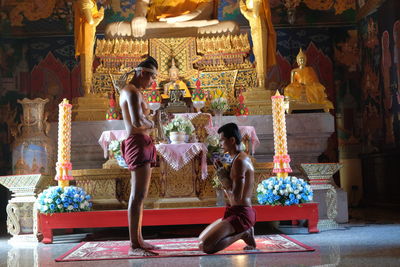 Side view of shirtless men praying in buddhist temple