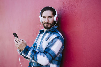 Portrait of young man using mobile phone against wall