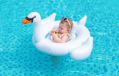 Baby girl eating fruit sitting on inflatable ring in pool