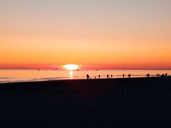 Silhouette people on beach against sky during sunset