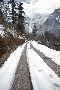 Snow covered road by mountains against sky