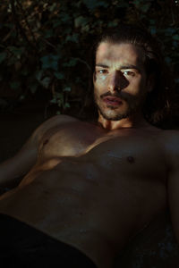 Portrait of shirtless wet young man lying in lake