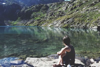 Rear view of man sitting on rock by lake