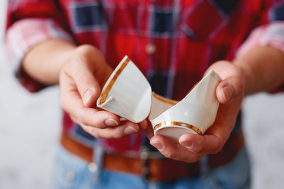 Man in plaid tartan shirt holds a broken white cup. damaged mug with golden decoration.