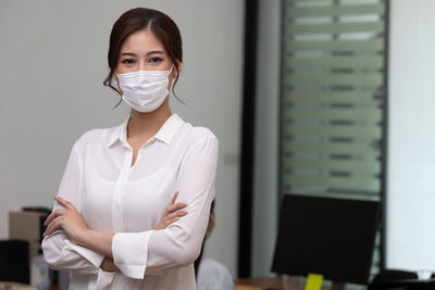 Portrait of businesswoman wearing mask gesturing while standing in office