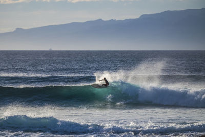 Teenager surfing on waves against sky