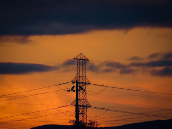 Low angle view of silhouette electricity pylon against dramatic sky