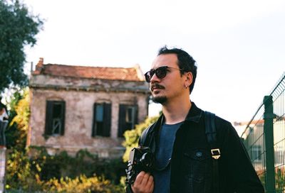 Man wearing sunglasses holding camera against clear sky