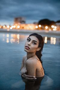 Portrait of woman standing against illuminated water