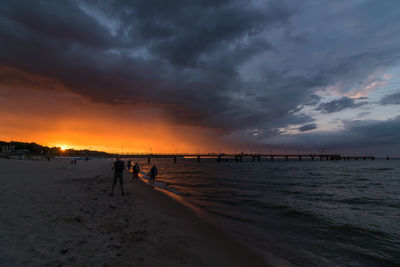 Silhouette people on beach against sky during sunset