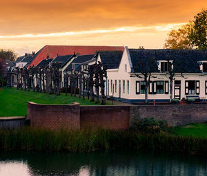 Houses by lake against sky during sunset