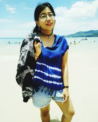 Young woman standing at beach against sky