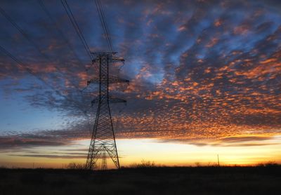 Silhouette electricity pylon against dramatic sky during sunset