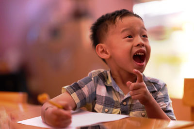 Boy with mouth open looking away while sitting at table