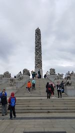 Low angle view of people at town square against cloudy sky