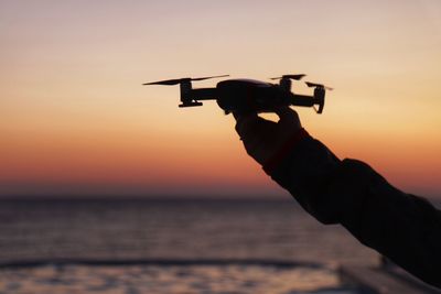 Cropped hand of woman holding drone against sea during sunset