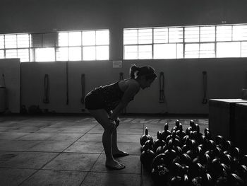 Side view of woman bending by kettlebells in gym