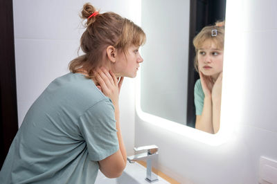 Teen girl looks in the mirror at problem skin in the bathroom