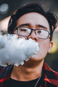 Portrait of man wearing eyeglasses blowing smoke from mouth outdoors