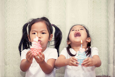 Sisters holding cupcakes against curtain during birthday