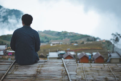 Rear view of silhouette man sitting on observation point against mountain