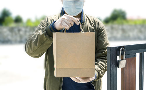 Midsection of delivery person holding bag standing outdoors