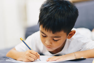 Cute boy writing in book at home