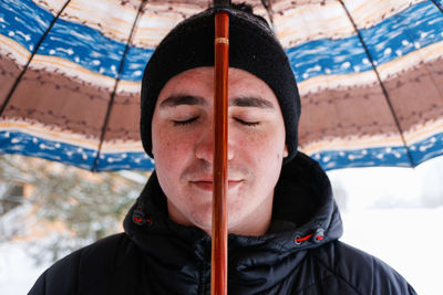 Portrait of young man with closed eyes in warm hat outside on rural winter snowy background holding