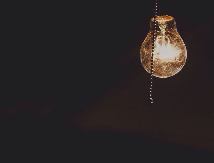 LOW ANGLE VIEW OF ILLUMINATED LIGHT BULB OVER BLACK BACKGROUND