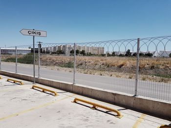 Road sign by fence against clear sky