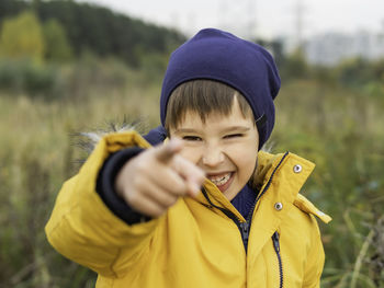 Smiling boy in yellow jacket points his finger at camera. laughing kid in park. fall season.