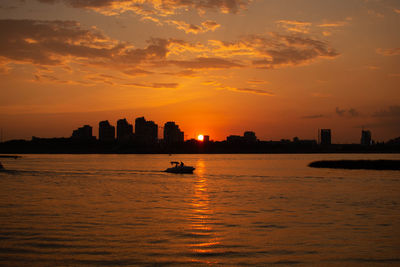 Silhouette buildings by sea against sky during sunset