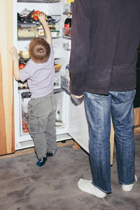 Father standing with curious son searching in refrigerator at home