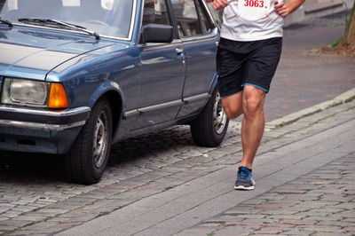 Low section of marathon athlete running by car on street