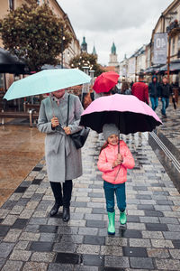 Mother and her little daughter holding the pink and blue umbrellas walking in a downtown