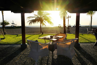 Chairs and table by palm trees on beach against sky