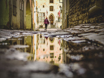 Reflection of woman standing on puddle against buildings