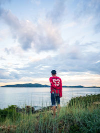 Rear view of man standing by sea against sky